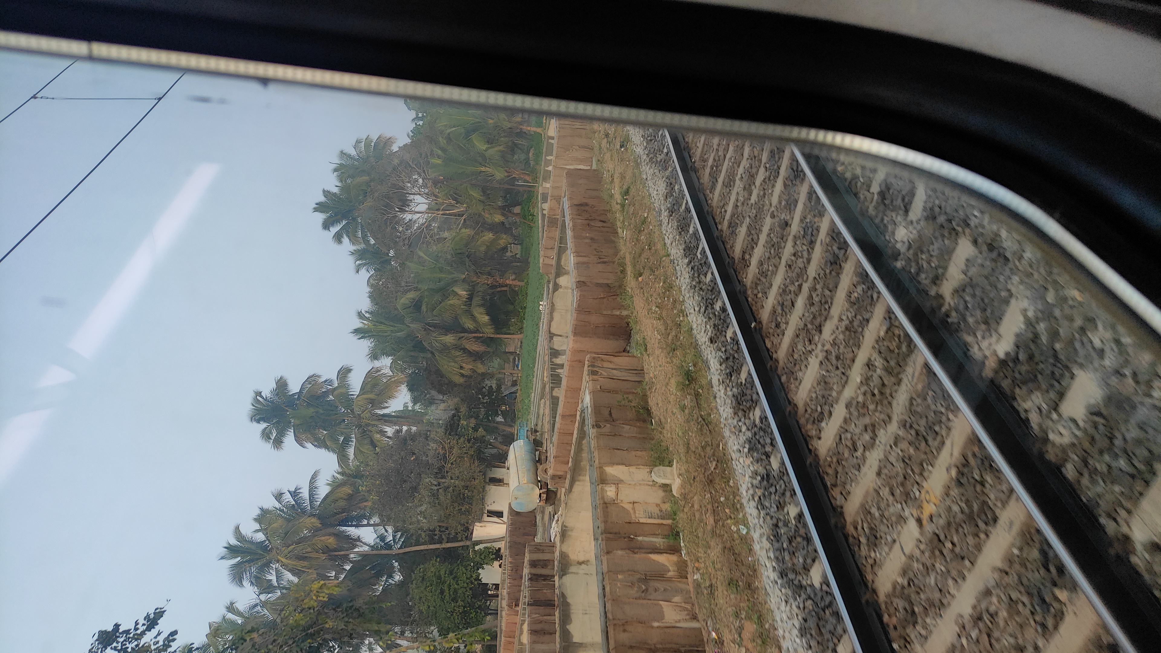 View from a train window showing railway tracks, trees, and a small structure in the background