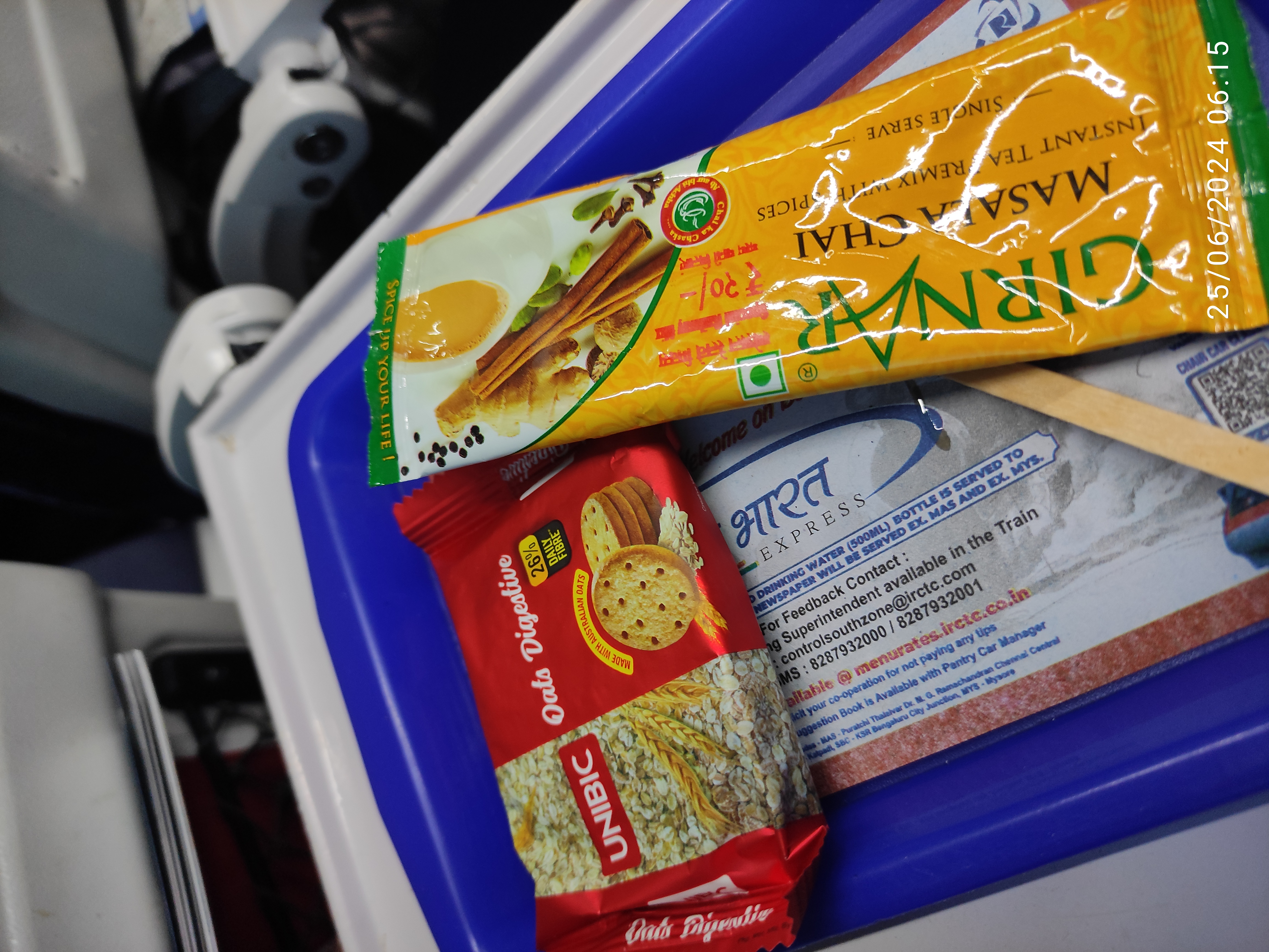 Packet of unibic biscuit, girnar tea pre-mix, stirrer on a blue tray